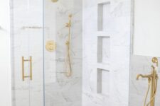 02 a beautiful neutral bathroom with a shower clad with white marble tiles, an oval tub, gold fixtures, a wooden stool