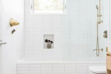 03 a bright bathroom with a mosaic floor, white tiles with built-in shelves, a window and gold hardware