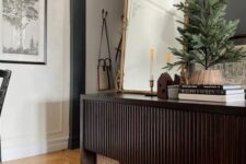 05 a beautiful dark-stained reeded console table with cane boxes under it, some coffee table books, an arched mirror and a Christmas tree