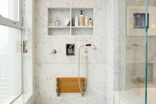 06 a chic shower space clad with white marble tiles, with niche with shelves used for storage, a folding seat, gold fixtures