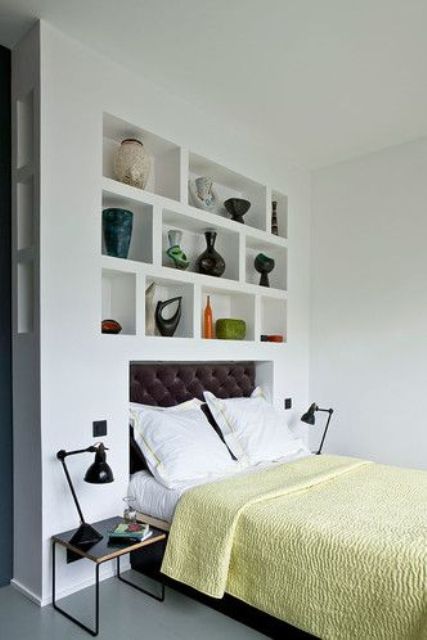 a modern bedroom with a headboard wall taken by niches with vases, a bed with a leather headboard and black nightstands and table lamps