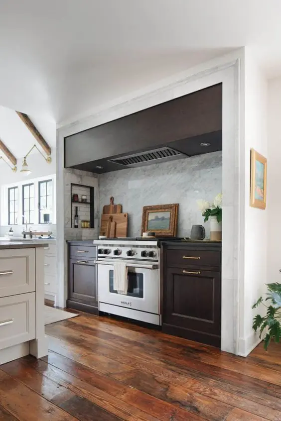 A modern farmhouse kitchen in white, with a large niche with dark stained cabinets and a hood, some small shelves for condiments and oils