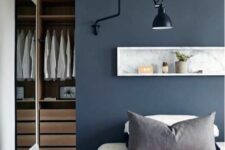 07 a modern bedroom with a navy accent wall and a long and narrow niche with decorations, a black sconce and a bed wiht neutral bedding