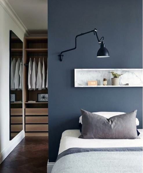 a modern bedroom with a navy accent wall and a long and narrow niche with decorations, a black sconce and a bed wiht neutral bedding
