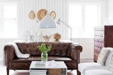 07 a refined rustic living room with a brown leather Chesterfield sofa, a vintage apothecary cabinet and white chairs