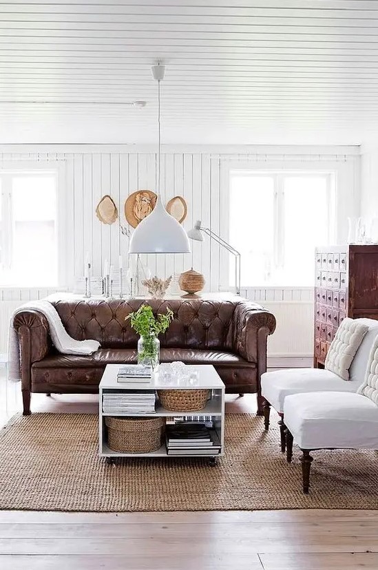 a refined rustic living room with a brown leather Chesterfield sofa, a vintage apothecary cabinet and white chairs