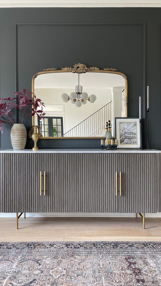 a chic sideboard with grey reeded doors, gold handles and legs, a refined mirror, some decor and candles for a lovely entryway