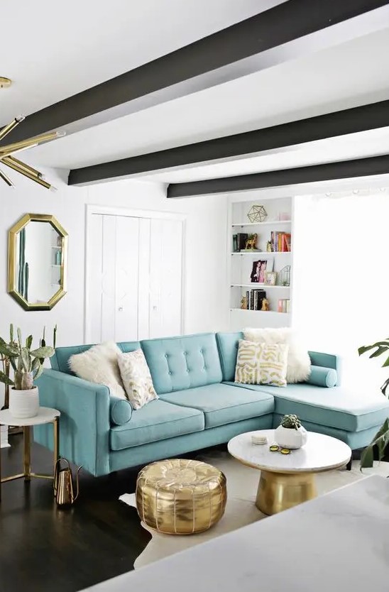 A beautiful mid century modern living room with a fireplace, dark beams on the ceiling, a modern turquoise sofa and touches of gold for more elegance