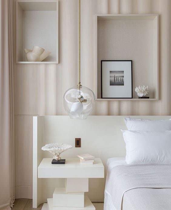 an airy neutral bedroom with a series of niches used for decor, a white bed and an architectural nightstand, a pendant lamp