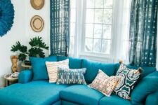 14 a bright living room with a turquoise sofa, a turquoise printed rug and curtains, decor on the wall and a carved wooden coffee table