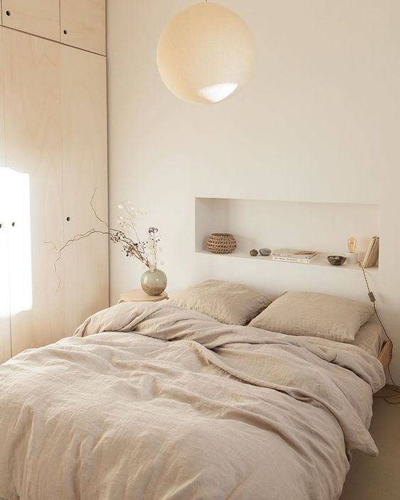 a serene Scandinavian bedroom with a timber wardrobe, a bed wiht neutral bedding and a headboard niche used for decorating the space