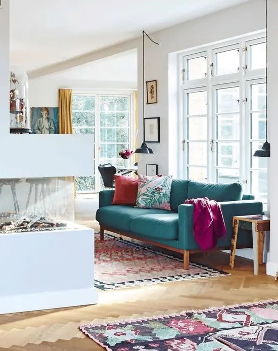 a contemporary living room with a fireplace, a modern turquoise sofa and bright textiles, pendant lamps and printed mini rugs