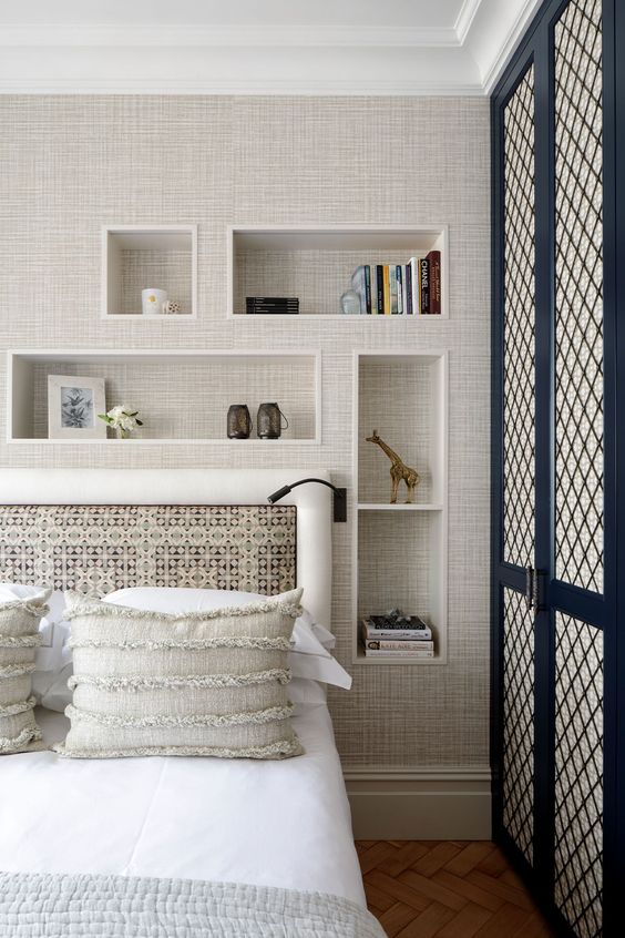 a chic bedroom with niche shelves with grasscloth wallpaper, a bed with a catchy bedding and a black sconce