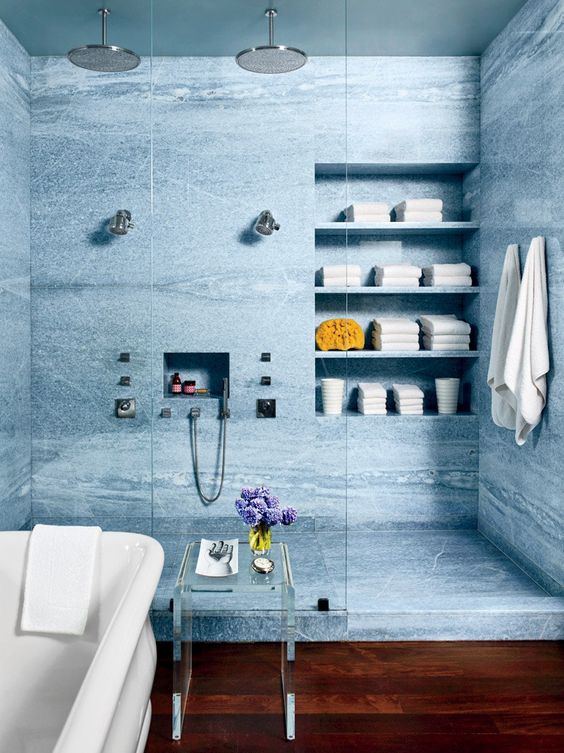 a large shower space clad with blue marble tiles, with a niche for towels and a niche for shampoos, a tub next to tit