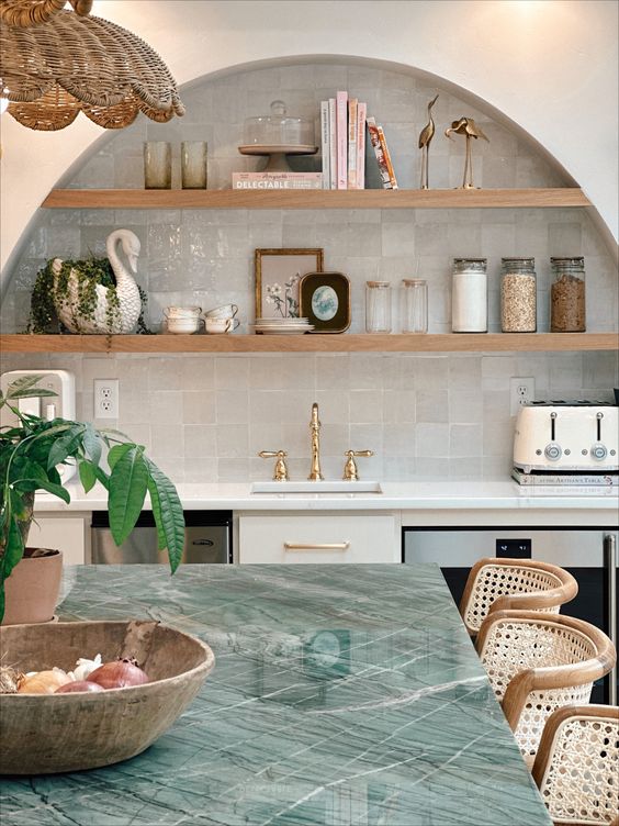 an arched niche clad with Zellige tiles and wooden shelves, some decor, books and jars  is a cool idea for a kitchen