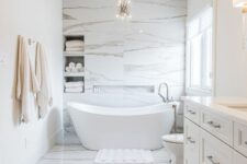 19 a minimalist luxurious bathroom clad with white marble, with niche shelves over the bathtub, an oval tub and a alrge vanity