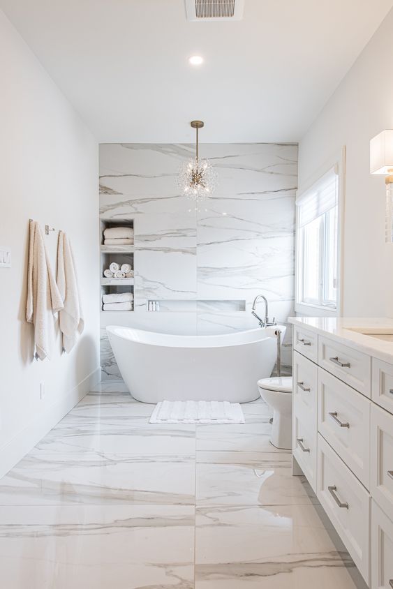 a minimalist luxurious bathroom clad with white marble, with niche shelves over the bathtub, an oval tub and a alrge vanity