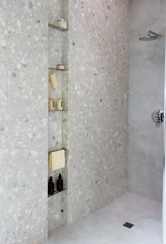 a minimalist shower space clad with stone tiles and with a long and narrow niche with metal shelves is a cool nook