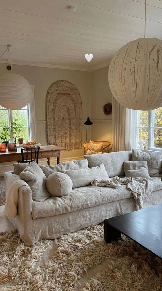 a catchy neutral living room with a linen sofa and pillows, a dark-stained coffee table, a fluffy rug, a wooden table and sphere pendant lamps
