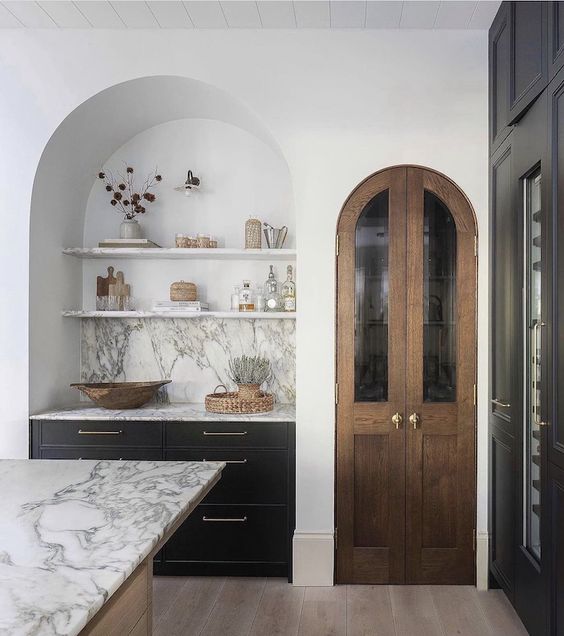 A contemporary kitchen with a large arched niche with built in dark cabinets, open shelves and a marble backsplash is adorable