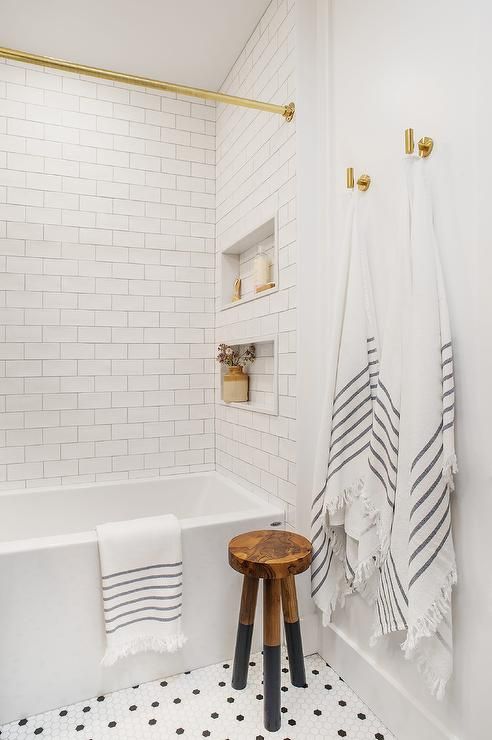 a modern farmhouse bathroom done with penny and subway tiles, with niches used for decor and storage and gold fixtures