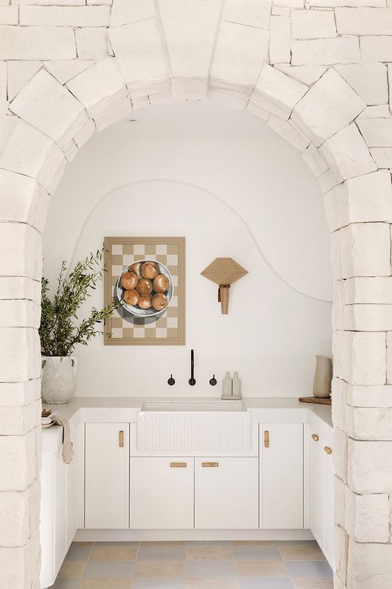 a large niche that contains the whole kitchen with sleek cabinets, stone countertops and a sink and some decor