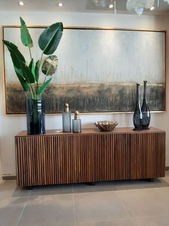 a refined rich-stained fluted console table with vases, bowls, fronds and an oversized artwork is amazing