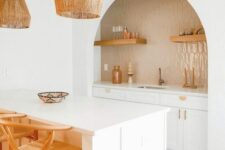 26 a lovely boho kitchen with white cabinets, an arched niche clad with tan tiles, open shelves, gold fixtures, pendant lamps
