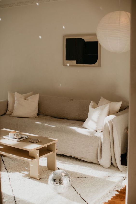 a neutral minimal living room with a linen sofa and pillows, a tiered coffee table, a disco ball and some decor