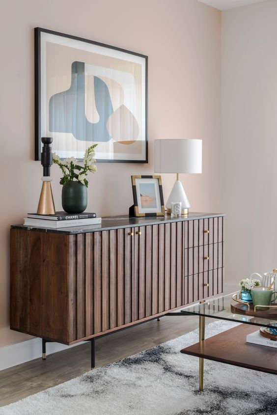 a rich-stained mid-century modern credenza with coffee table books, some lamps and decor and blooms is wow