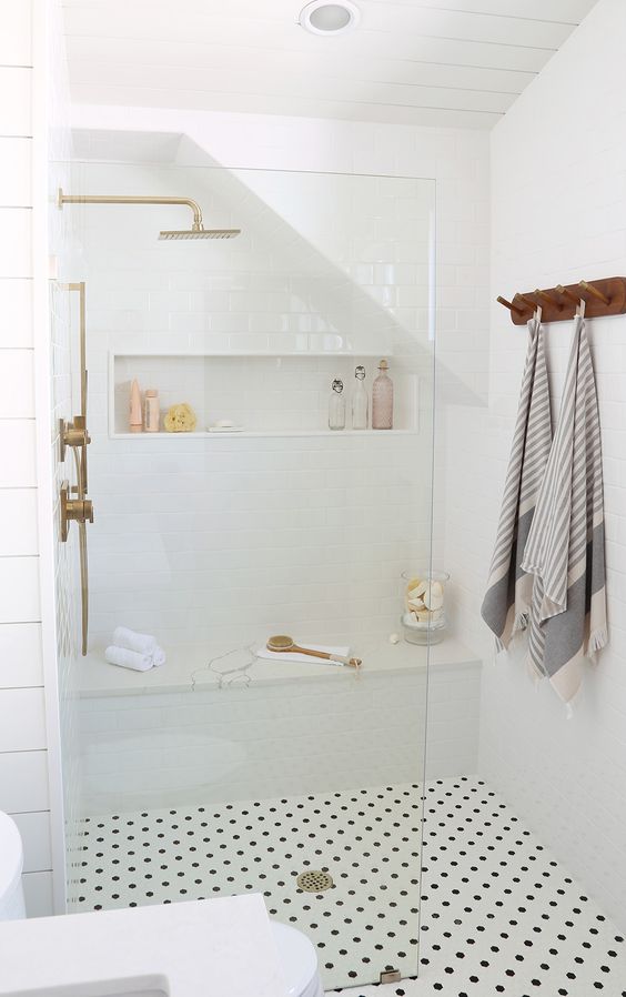 a modern neutral bathroom clad with white tiles and penny ones, with a built-in bench and a niche shelf for storage