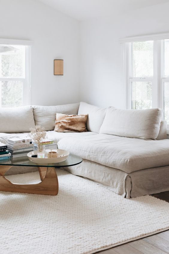 a neutral living room with a linen sectional and linen pillows, a coffee table with decor and books