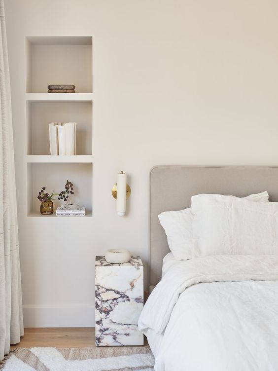 a neutral serene bedroom with a bed, a marble nightstand and niche shelves used fro storage and decor