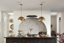 28 a modern kitchen with an arched niche clad with Zellige tiles and built-in cabinets, a black kitchen island, brass pendant lamps and industrial stools