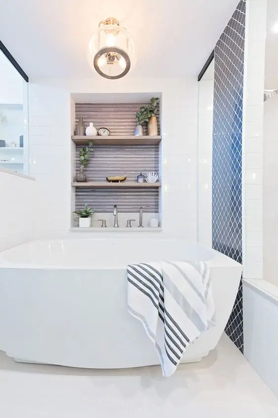 a modern neutral bathroom with a navy tile accent wall, a large tub, a niche clad with wood and shelves used for decorating