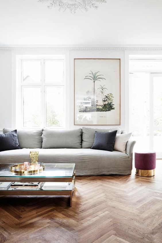a chic living room with a grey linen sofa and pillows, a mauve pouf, a tiered coffee table and a bold artwork