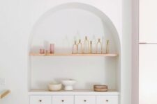 29 a modern kitchen with an arched niche that accommodates white cabinets, an open shelf and some objects stored and displayed
