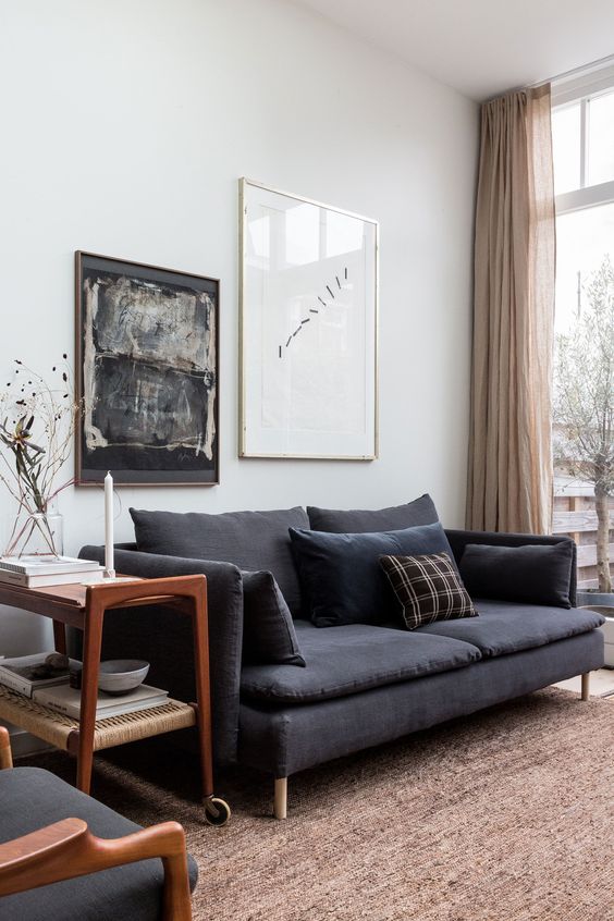 A chic mid century modern living room with a black linen sofa, a tiered trolley, a rug, some chairs and a mini gallery wall