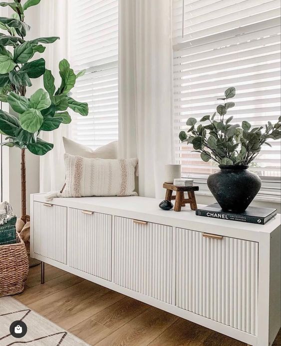 a white fluted credenza with pillows, a book and some lovely decor plus a potted plant next to it is a cool idea
