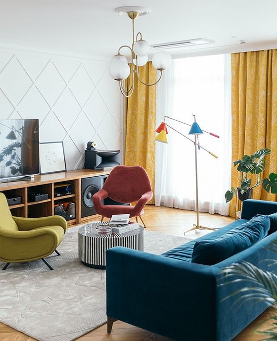 A bright mid century modern living room with a stained storage unit, a coral and mustard chair, a navy sofa, a side table and colorful lamps