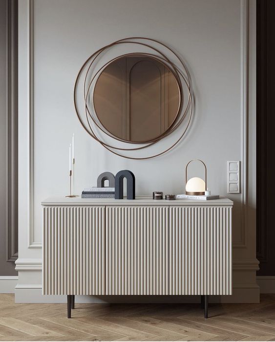 an elegant space with a round mirror with a creative frame, a neutral fluted sideboard with decor on tall legs