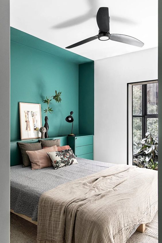 A catchy bedroom with a large window, a large niche painted emerald with a bed in it and built in nightstands