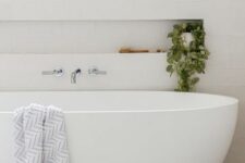 35 a neutral minimal bathroom clad with white subway tiles, with an oval tub, a niche shelf that is used mostly for decor