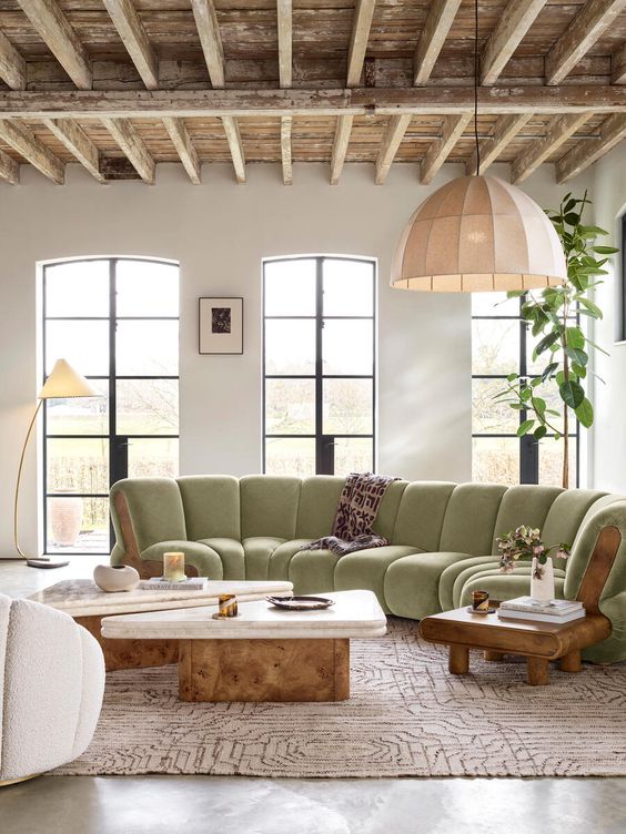 a refined living room with tall windows, a light green cotton sectional, a duo of coffee tables, a couple of chairs