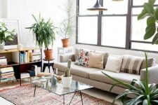 37 a modern boho living room with a neutral cotton sofa, printed rugs, a bookshelf, a glass coffee table, black pendant lamps and potted plants