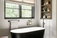 37 a neutral modern farmhouse bathroom clad with shiplap, with an oval black tub, a timber niche with shelves used for decor