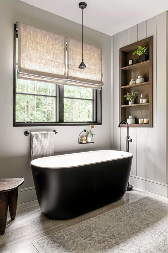 a neutral modern farmhouse bathroom clad with shiplap, with an oval black tub, a timber niche with shelves used for decor