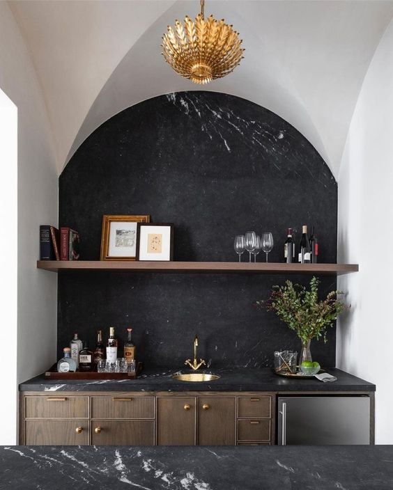 An exquisite kitchen with dark stained cabinets and a kitchen island, black marble countertops and a backsplash, an arched niche that accommodates part of the cabinetry