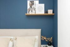 38 a modern bedroom with a large niche painted navy, a neutral bed with bedding in it, a shelf and a white nightstand