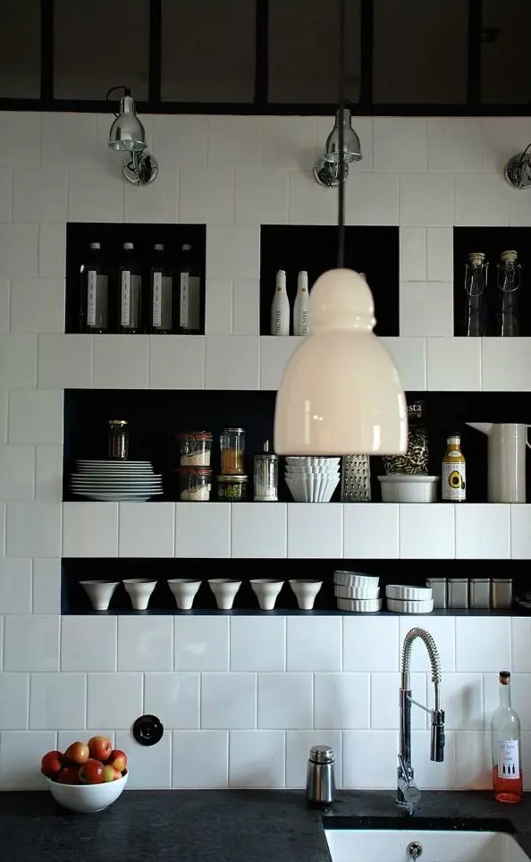 a creative black and white kitchen with square tiles and niche shelves that are used instead of upper cabinets for storing various tableware